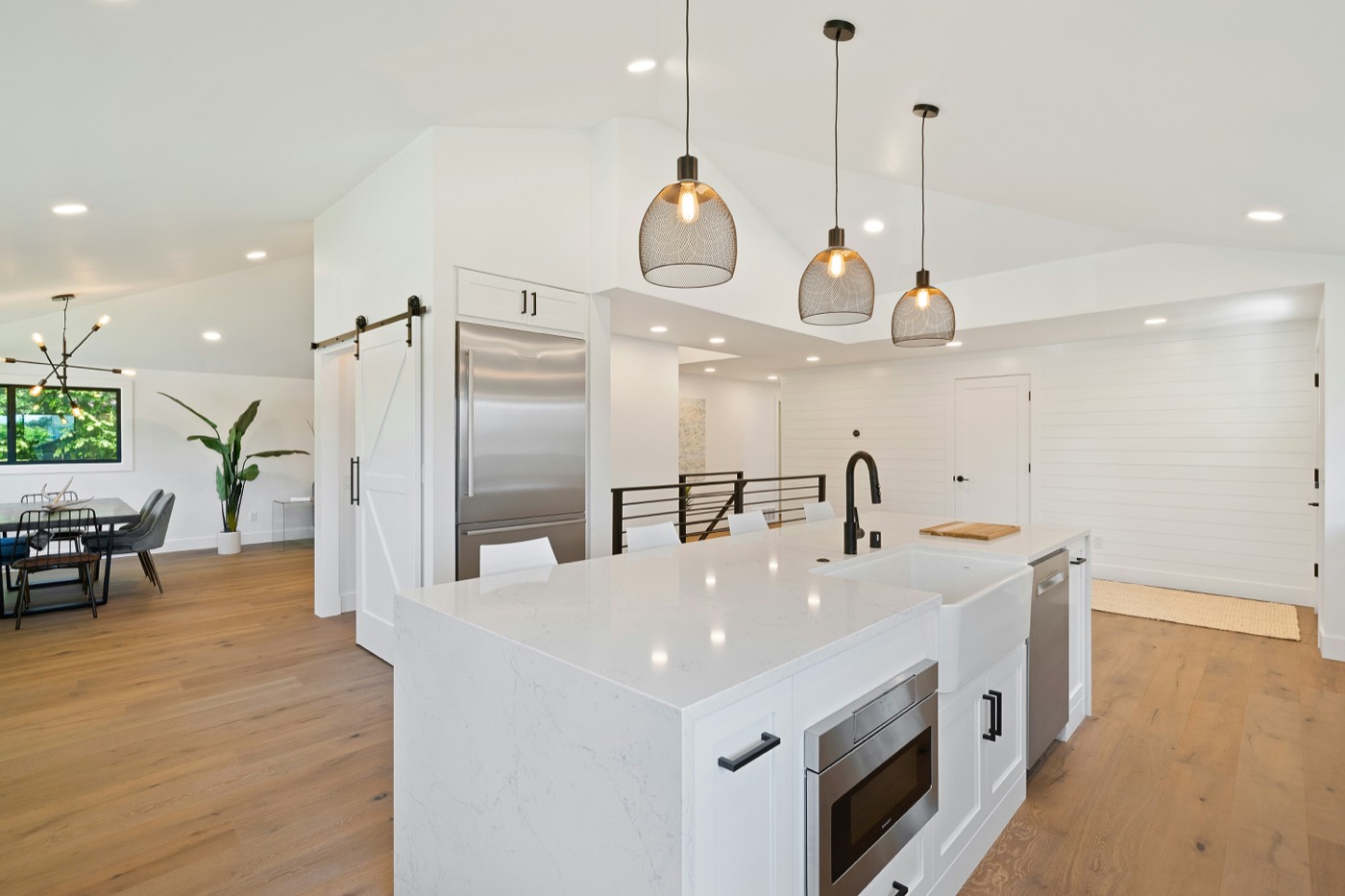 Open-plan kitchen with a white stone island, three pendant lights and a dining area beyond